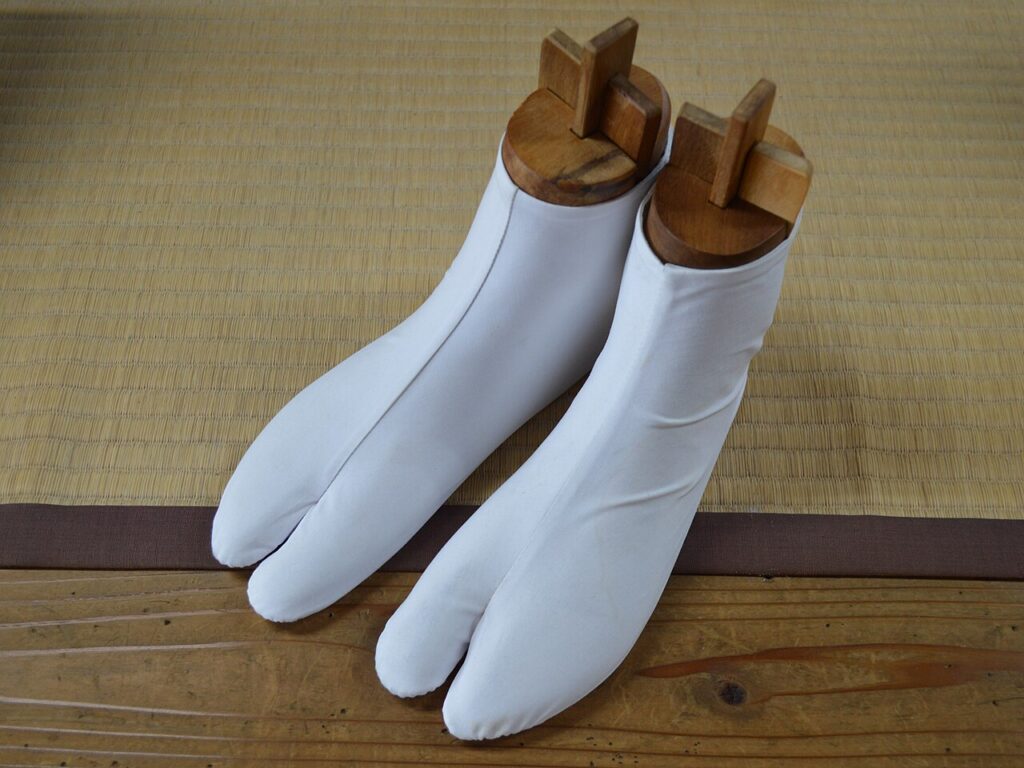 나무 틀에 씌운 흰색 타비 양말 한 쌍으로, 엄지발가락 부분이 나머지 발가락과 갈라져 있다.