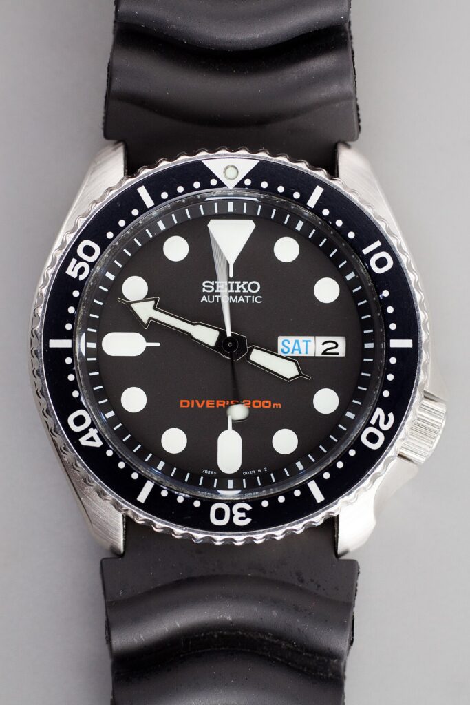 검은 고무 스트랩을 단 세이코 SKX007의 다이얼 확대 사진. 흰색 눈금과 시침·분침, 움직임이 겹쳐 보이는 가느다란 초침이 보인다.