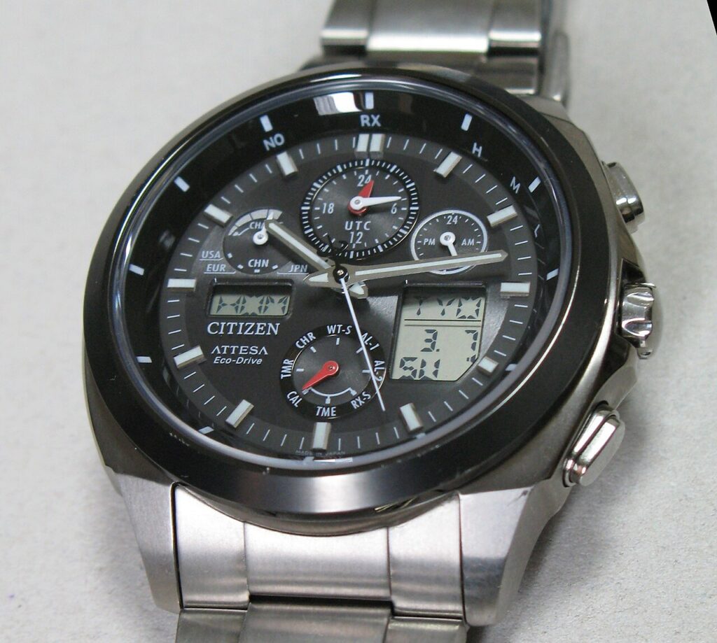 검은 다이얼과 금속 줄의 시티즌 Attesa Eco-Drive 시계로, 케이스 오른쪽에 용두와 위아래 누름 버튼이 보이는 모습