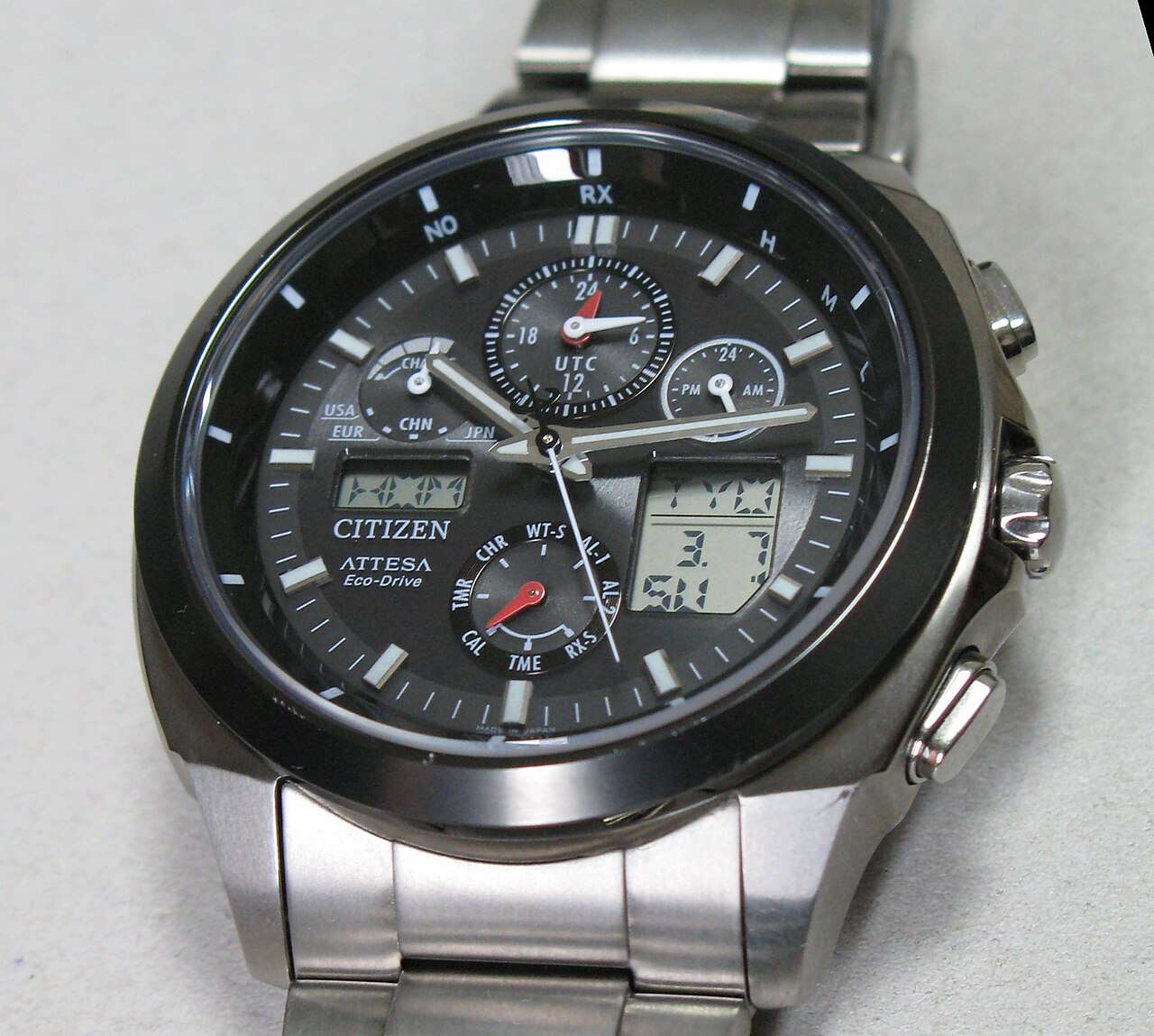 검은 다이얼과 금속 줄의 시티즌 Attesa Eco-Drive 시계로, 케이스 오른쪽에 용두와 위아래 누름 버튼이 보이는 모습